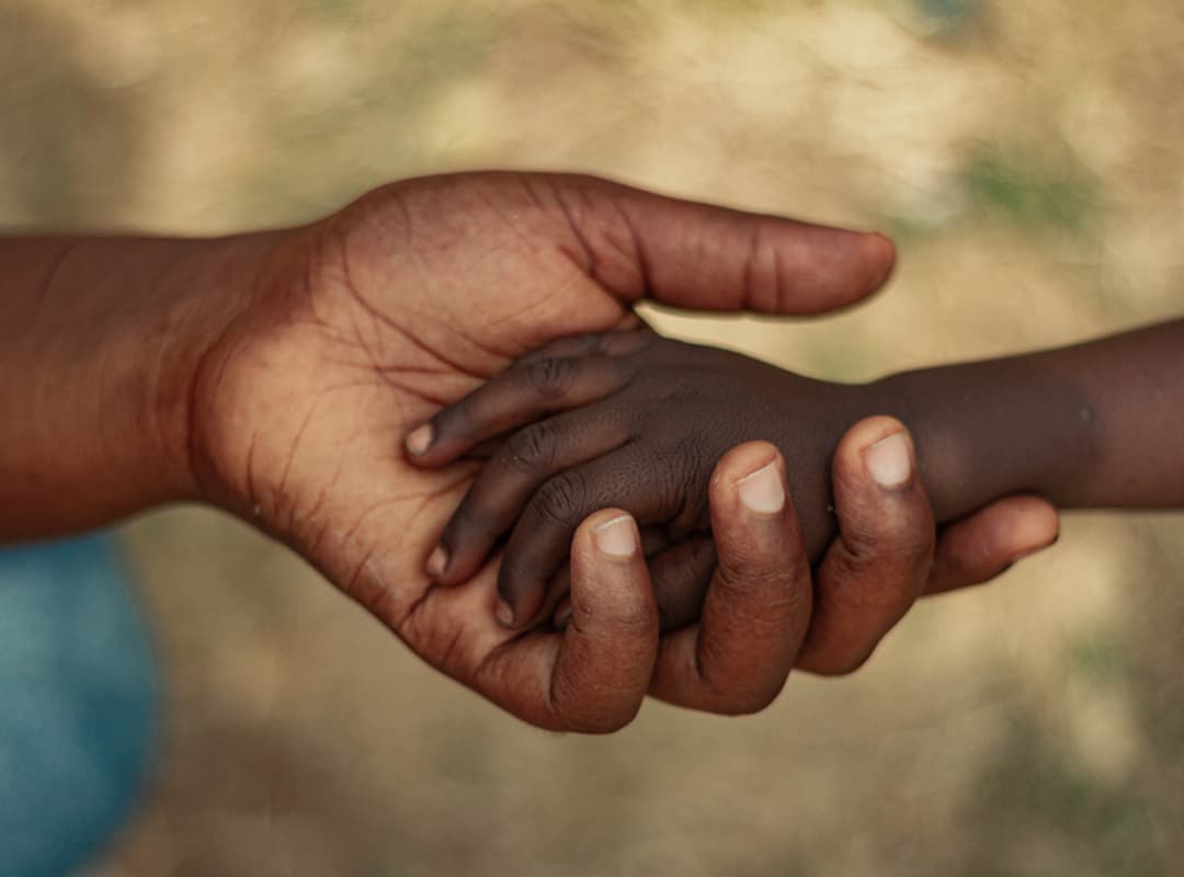 Mains d'un adulte soutenant la main d'un enfant — symbole de protection et de solidarité